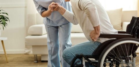 Physical disability. Nice sad aged man holding a caregivers hand and trying to get up while having a physical disability